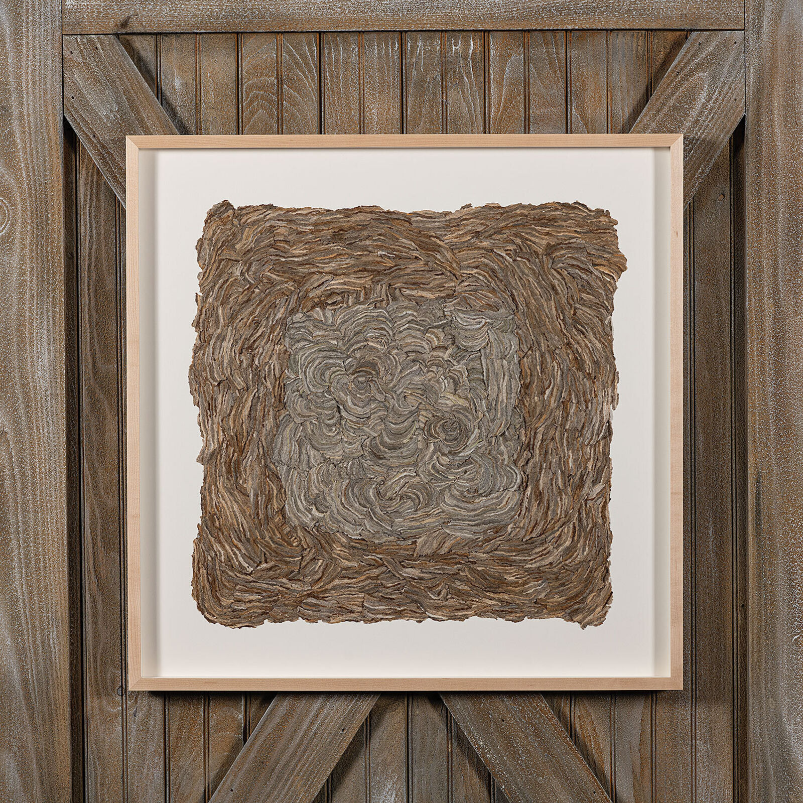 A framed square artwork featuring a textured, swirled surface in earthy tones.