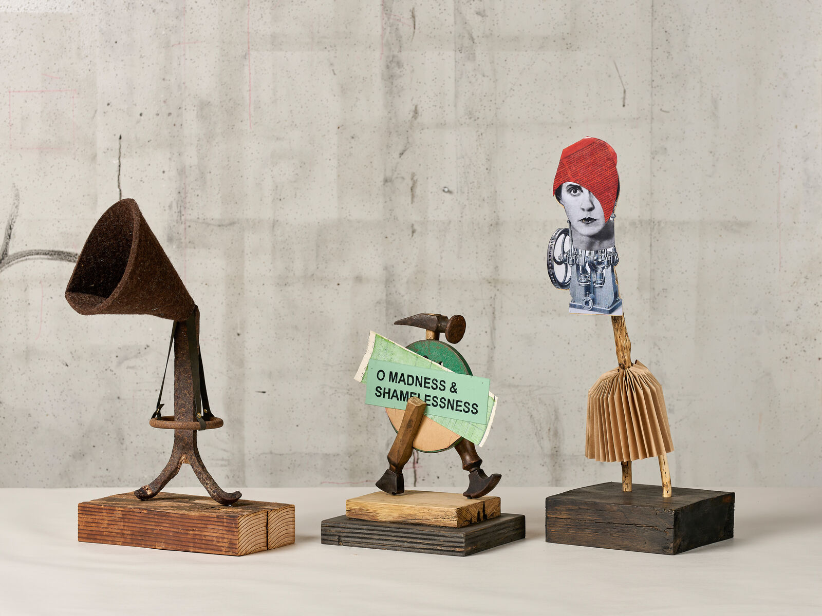 Three wooden sculptures of a man with a red hat and a broom.