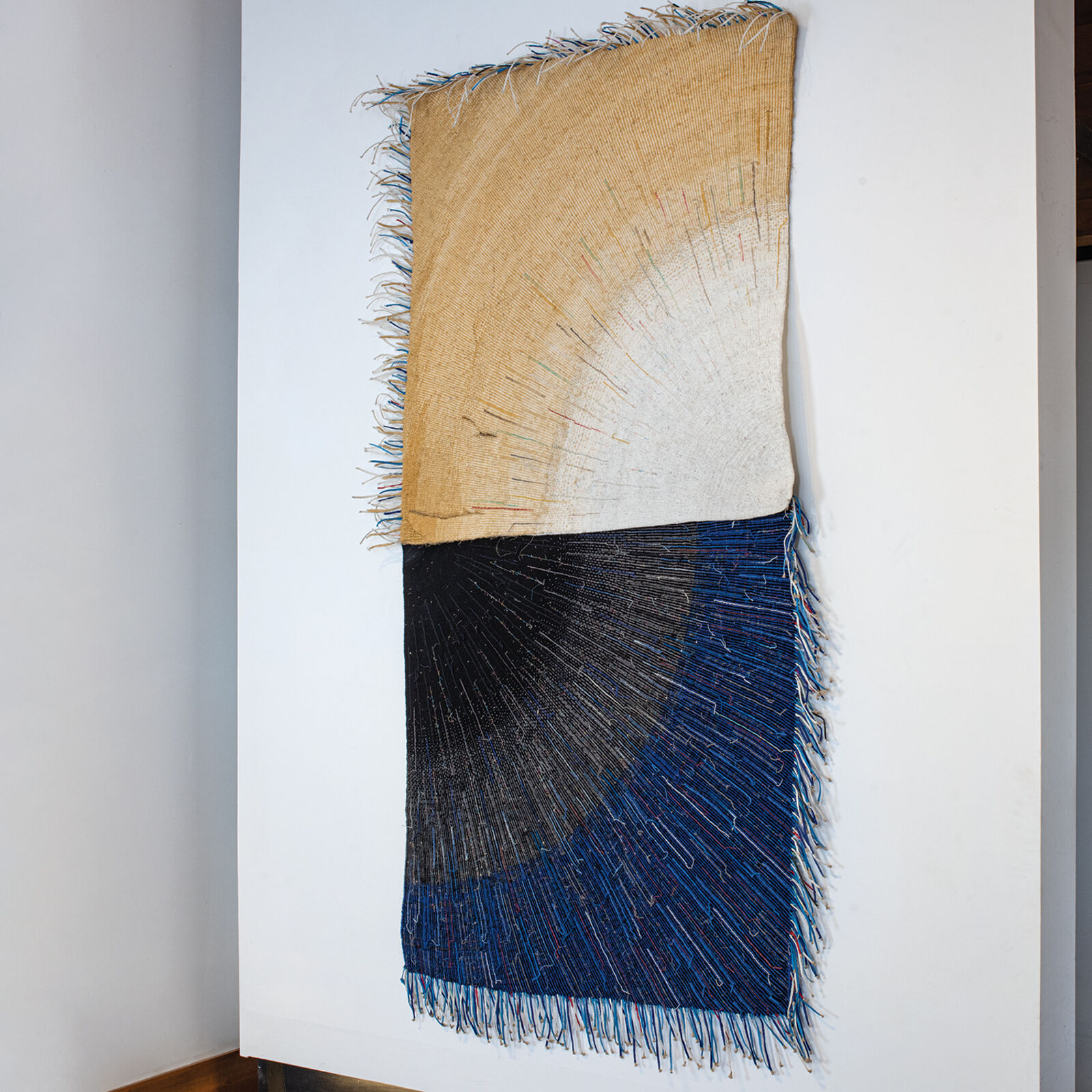 A textile artwork featuring a vertical split between earthy and deep tones, with radiating thread patterns.