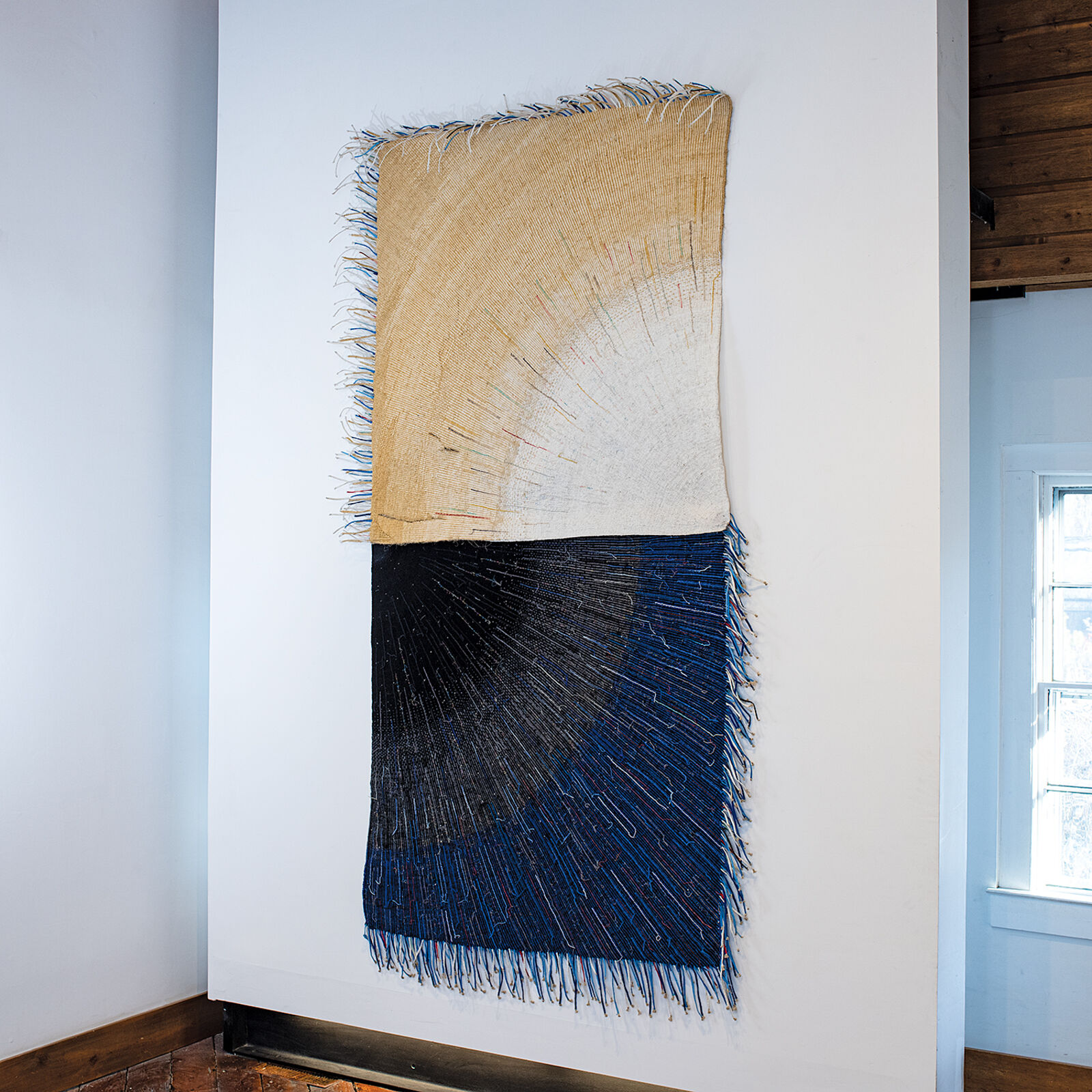 A textile artwork featuring a vertical split between earthy and deep tones, with radiating thread patterns.