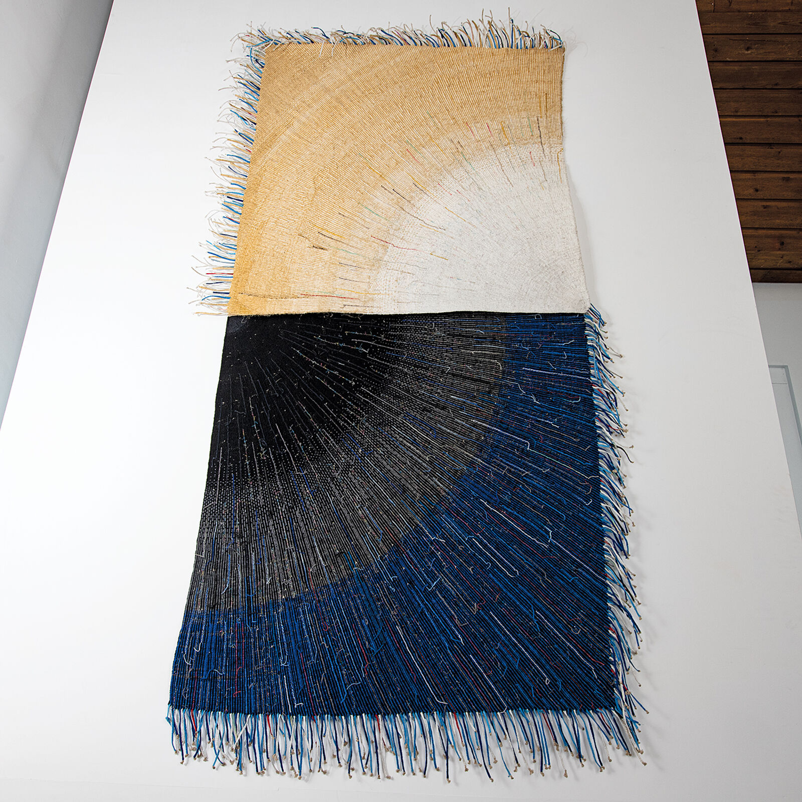 A textile artwork featuring a vertical split between earthy and deep tones, with radiating thread patterns.