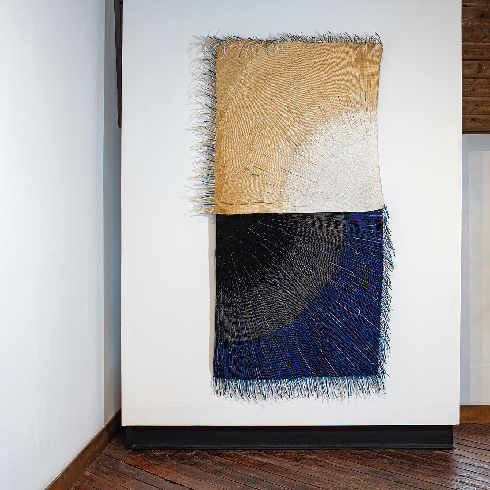 A textile artwork featuring a vertical split between earthy and deep tones, with radiating thread patterns.