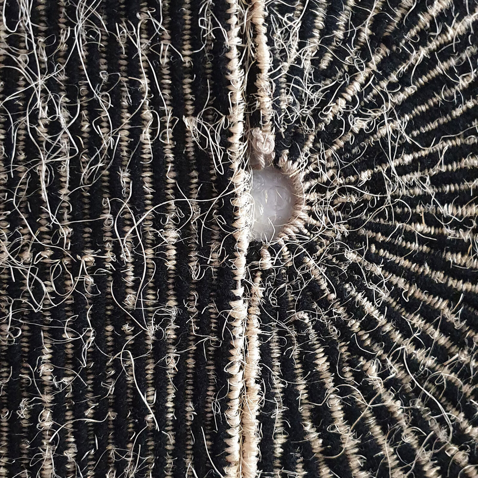 A minimalist textile artwork featuring a sunburst pattern emerging from a horizontal horizon line.