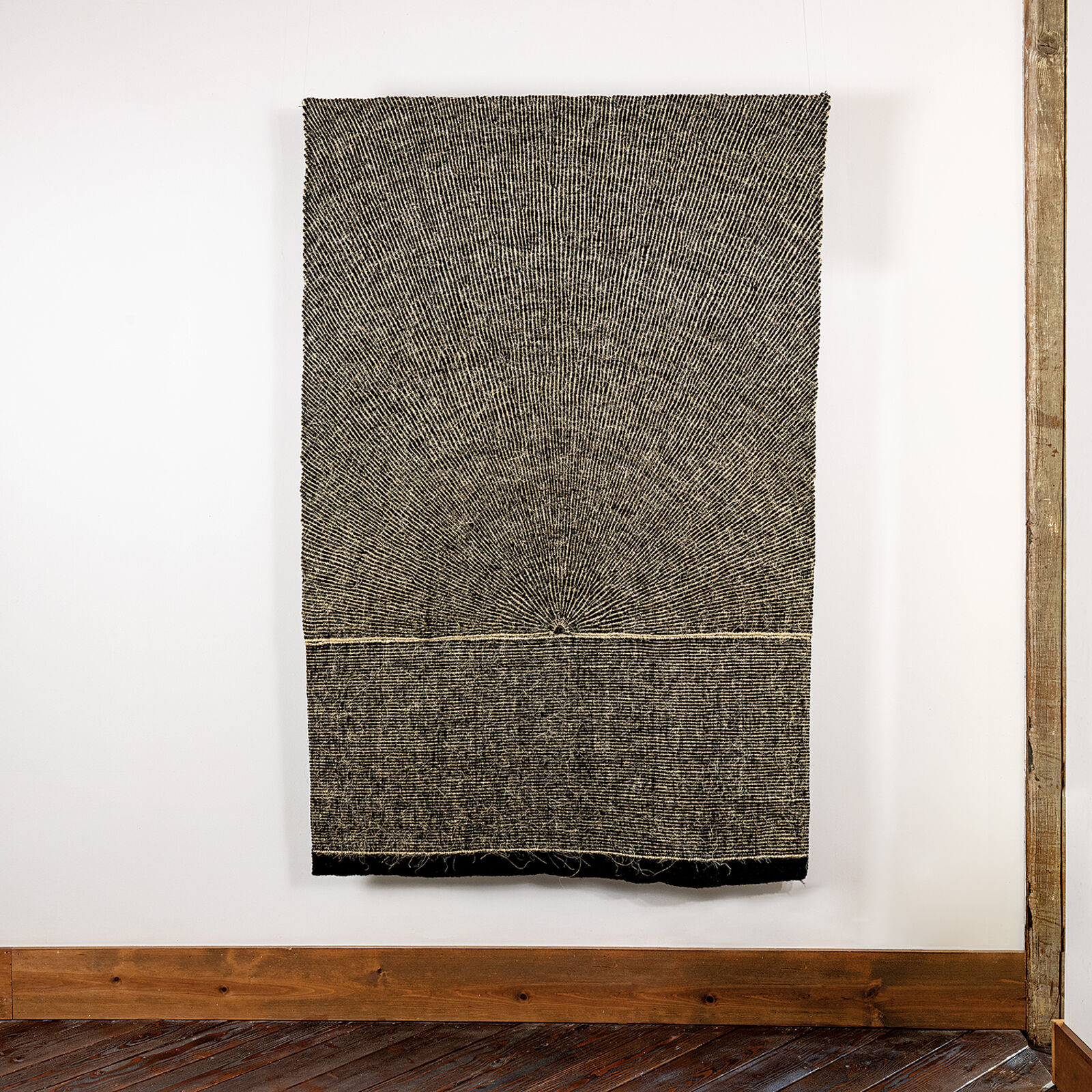 A minimalist textile artwork featuring a sunburst pattern emerging from a horizontal horizon line.