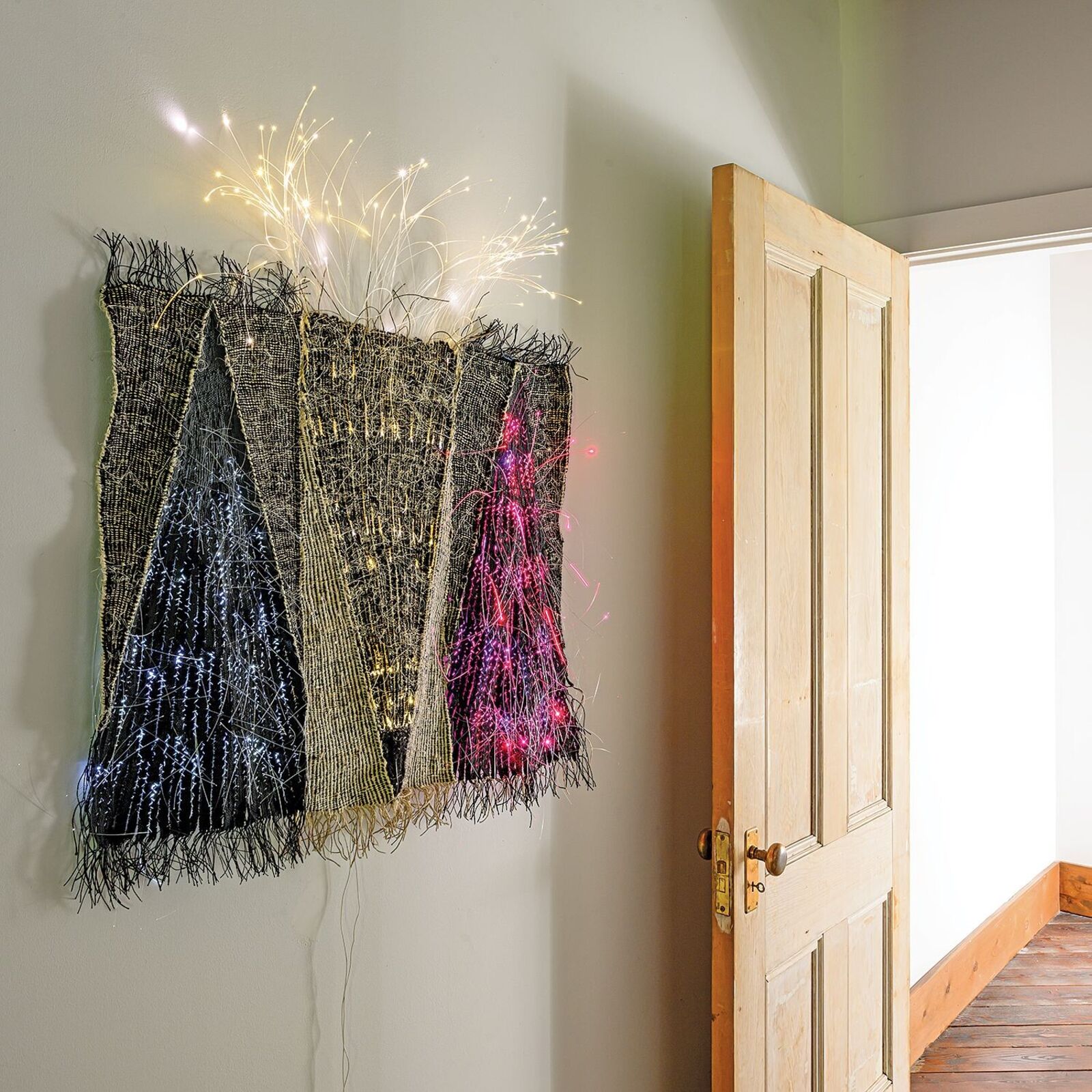 A woven textile artwork featuring three triangular shapes with embedded lights.