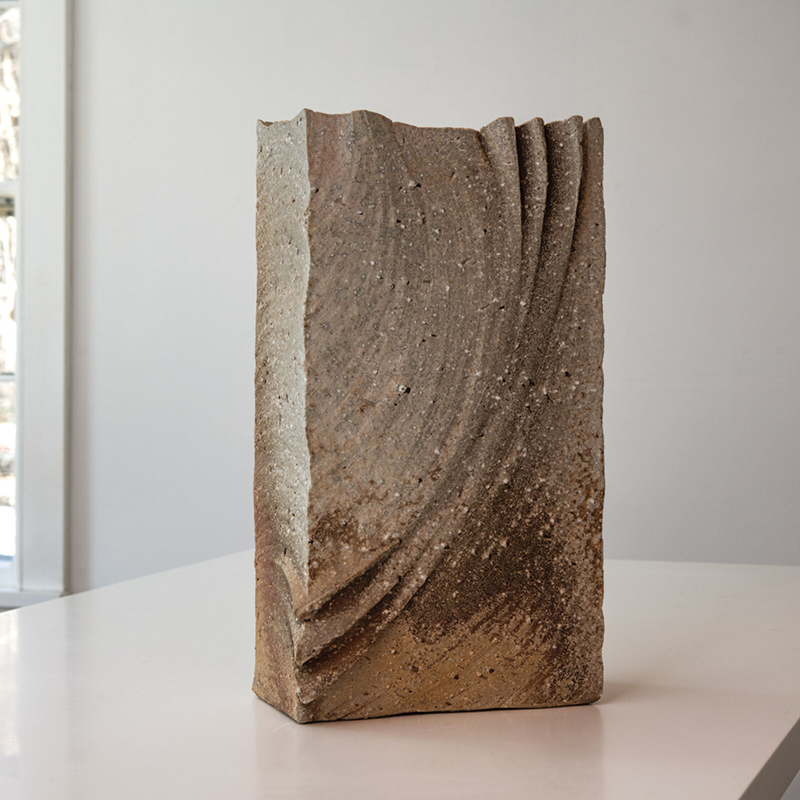 A textured, folded stone sculpture resting on a white surface.