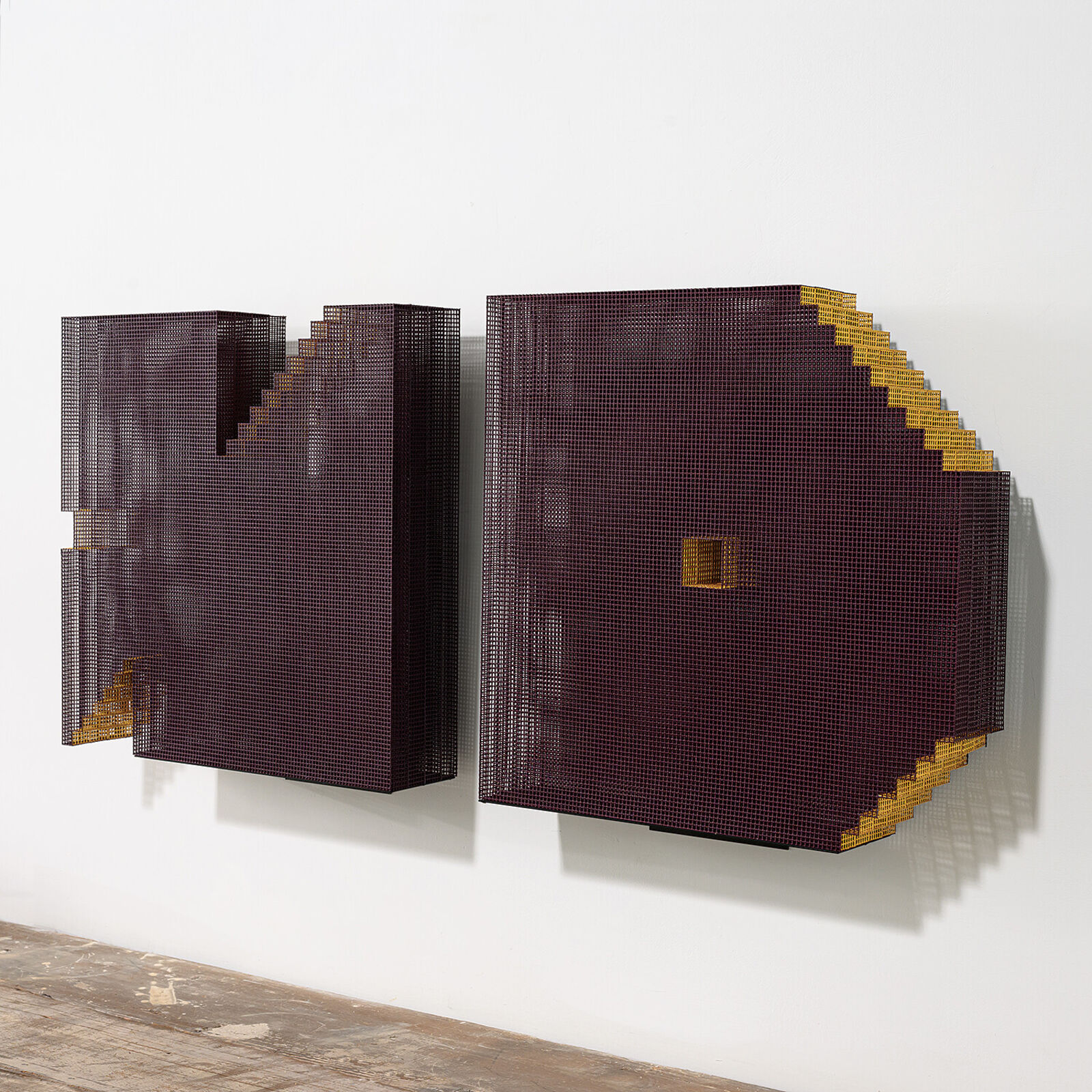 A minimalist installation featuring two pixelated, maroon-colored panels mounted on a white wall above a weathered wooden shelf.