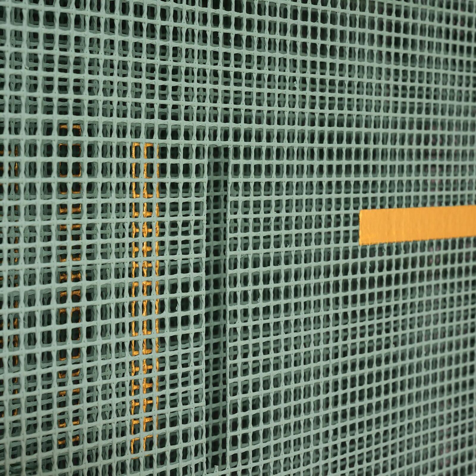 A green mesh sculpture with yellow and black geometric accents mounted on a white wall.