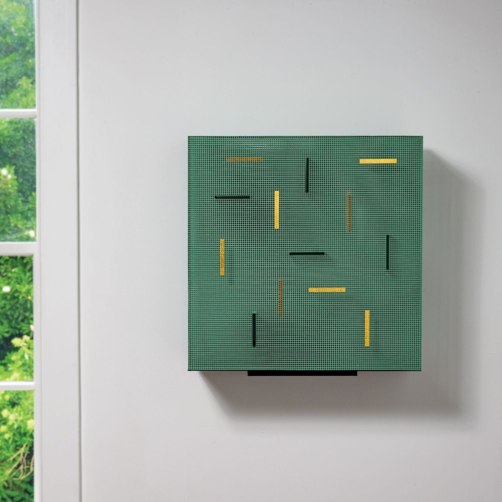 A green mesh sculpture with yellow and black geometric accents mounted on a white wall.