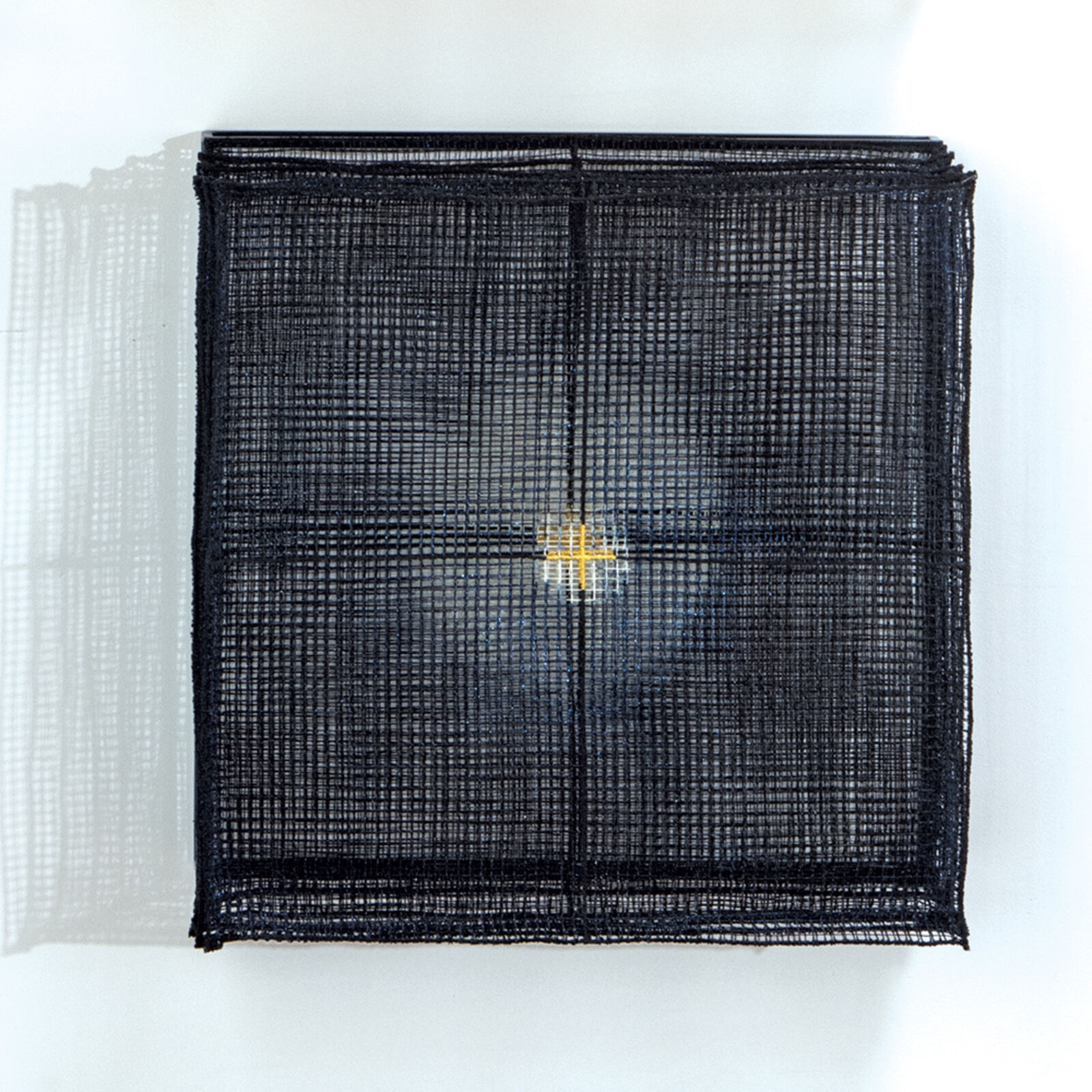 A minimalist textile artwork featuring a black woven square with a central yellow cross.