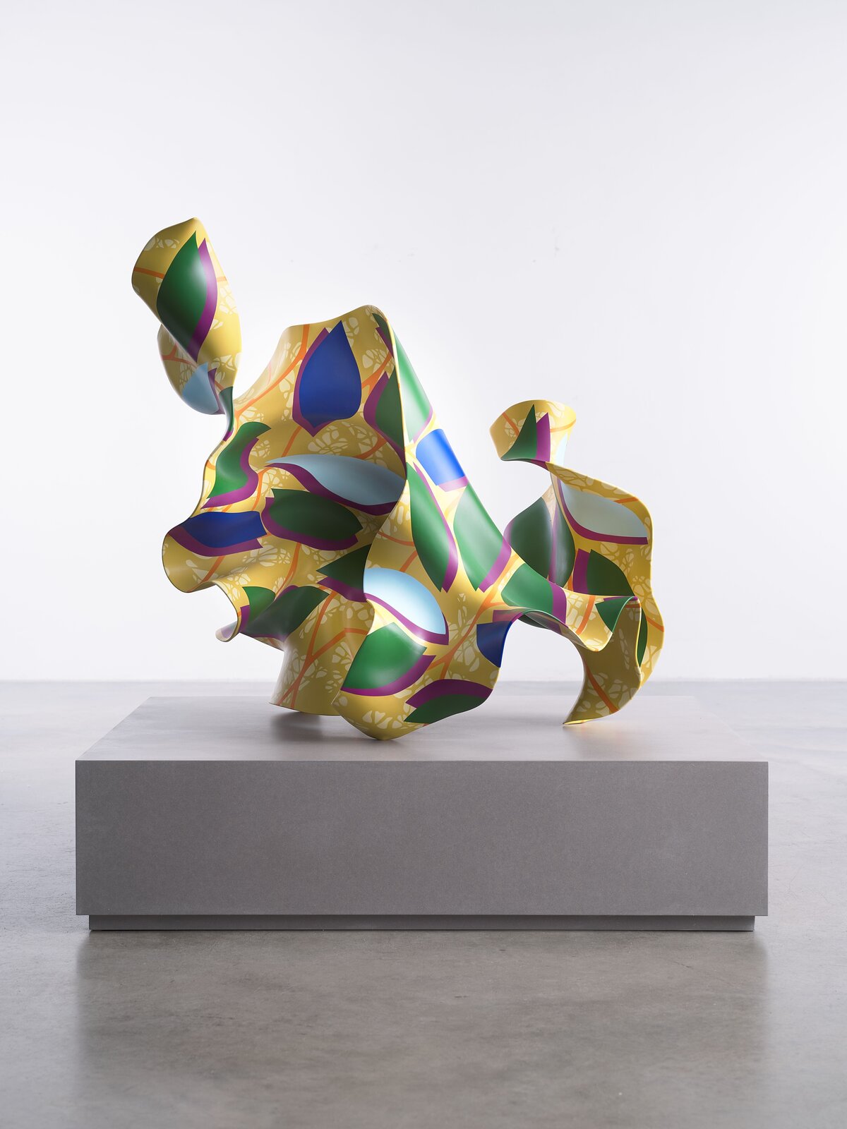 A colorful abstract sculpture with organic, flowing forms resting on a gray pedestal.