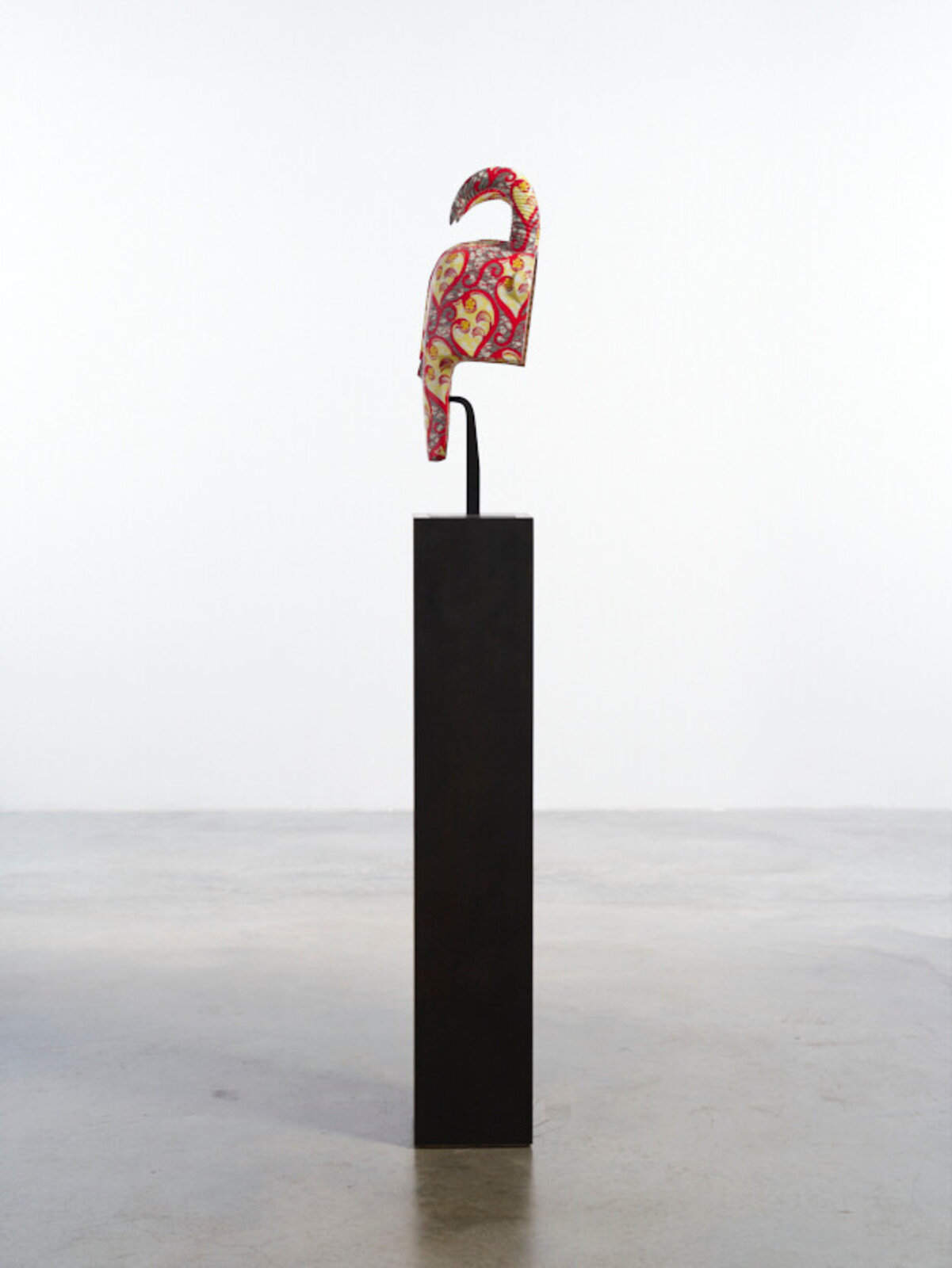 A colorful, patterned mask with curved horns displayed on a black pedestal.