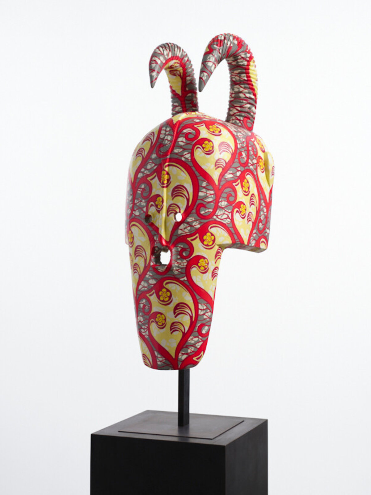 A colorful, patterned mask with curved horns displayed on a black pedestal.