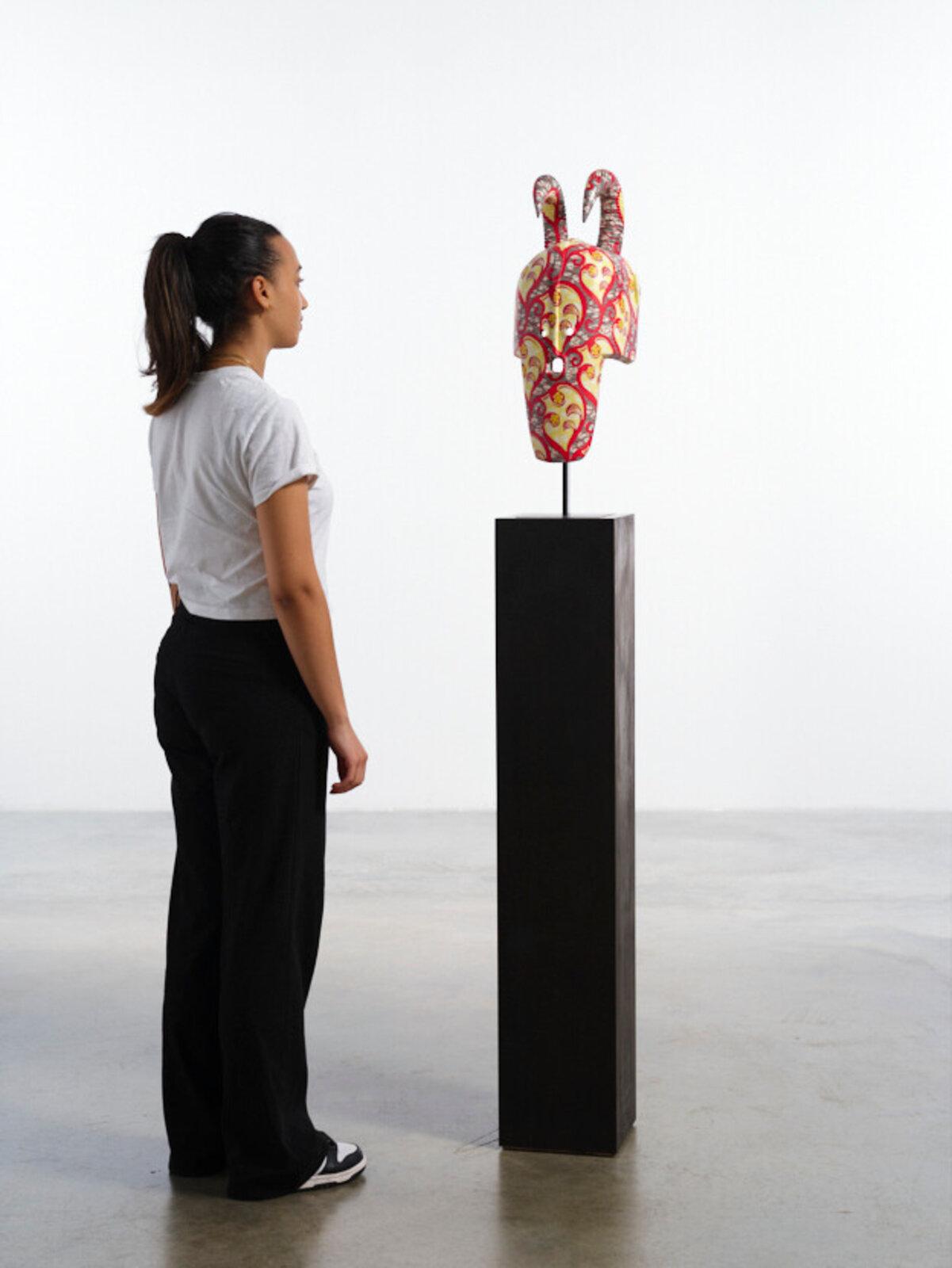 A colorful, patterned mask with curved horns displayed on a black pedestal.