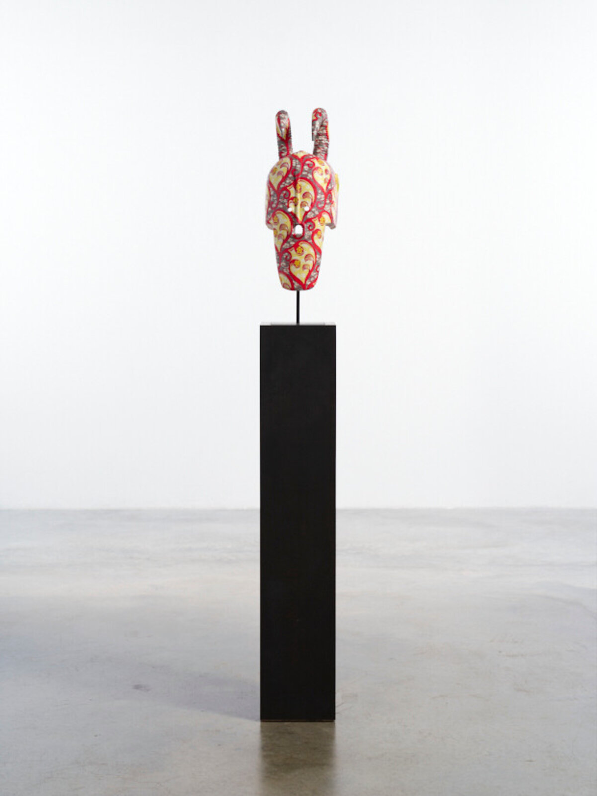 A colorful, patterned mask with curved horns displayed on a black pedestal.