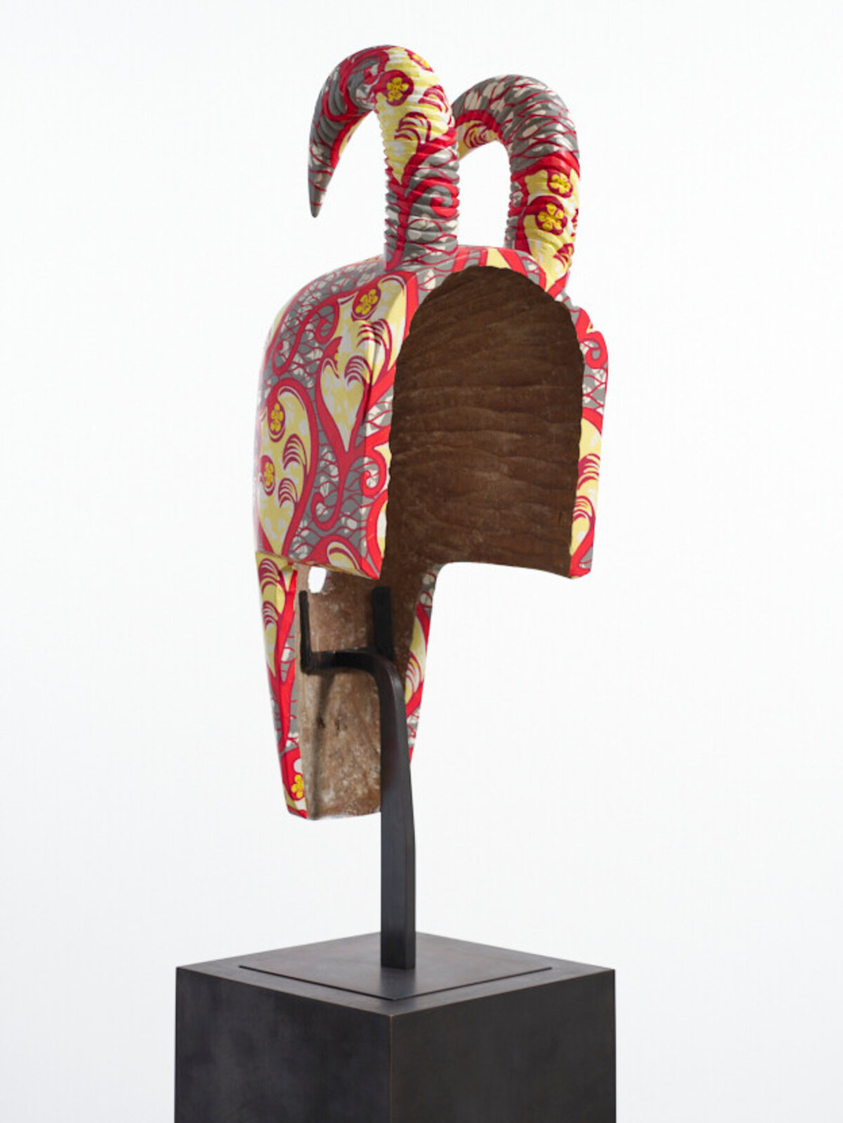 A colorful, patterned mask with curved horns displayed on a black pedestal.