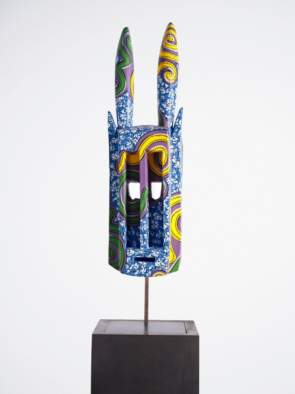 A blue and yellow mask on a wooden stand.