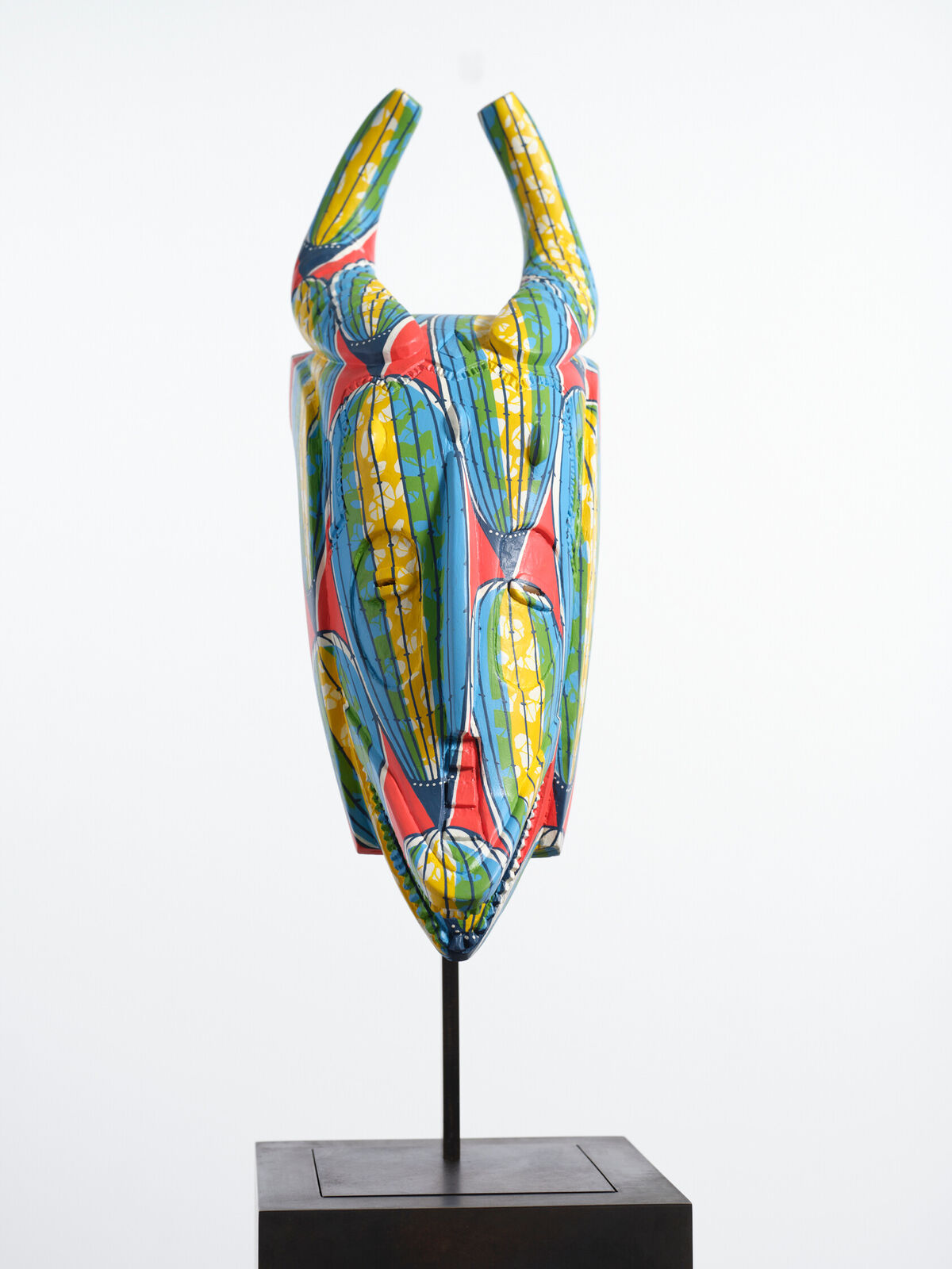 A colorful mask on a metal stand on a white background.