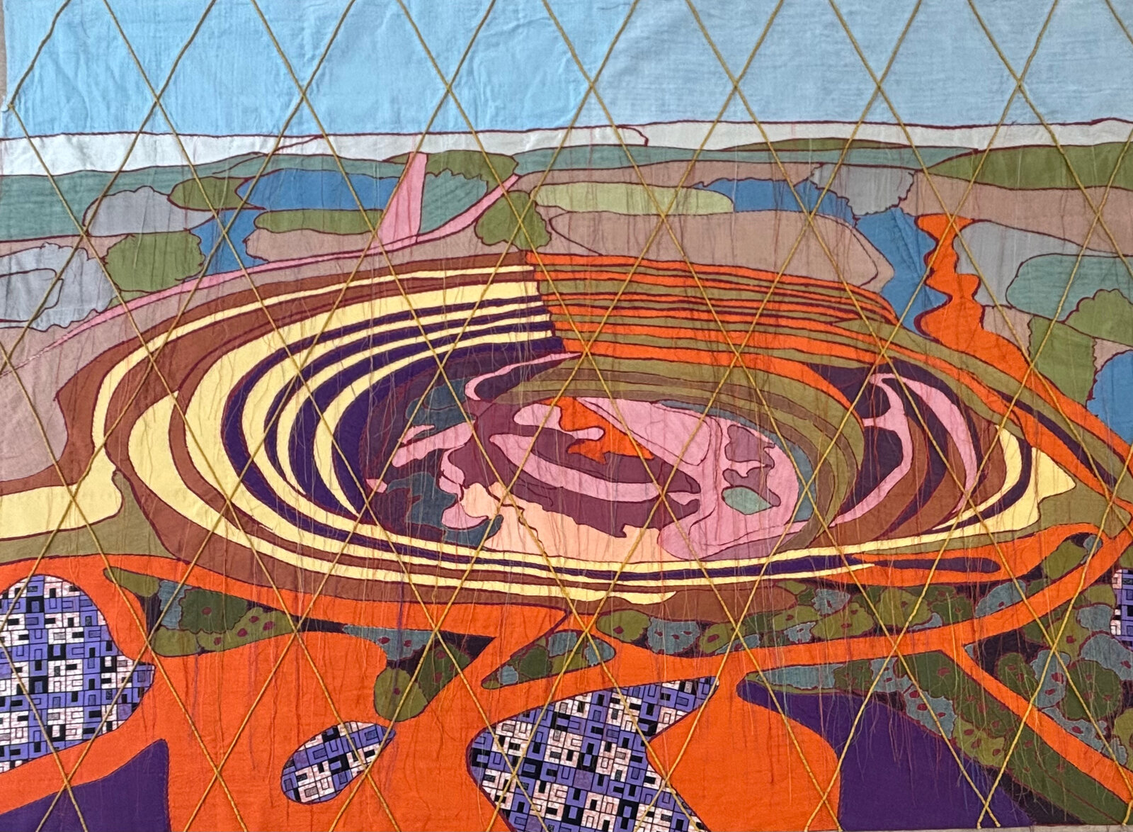 A colorful quilted textile featuring a swirling landscape with geometric stitching.