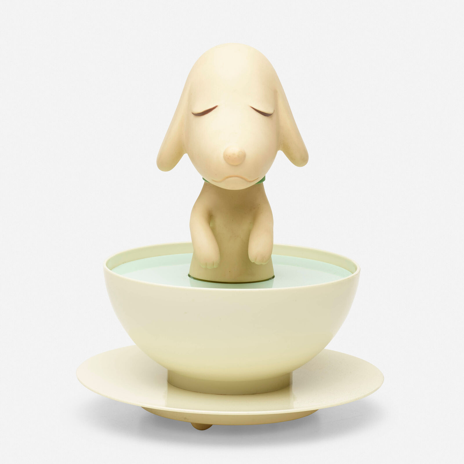 A small figurine of a dog sitting in a bowl of water.