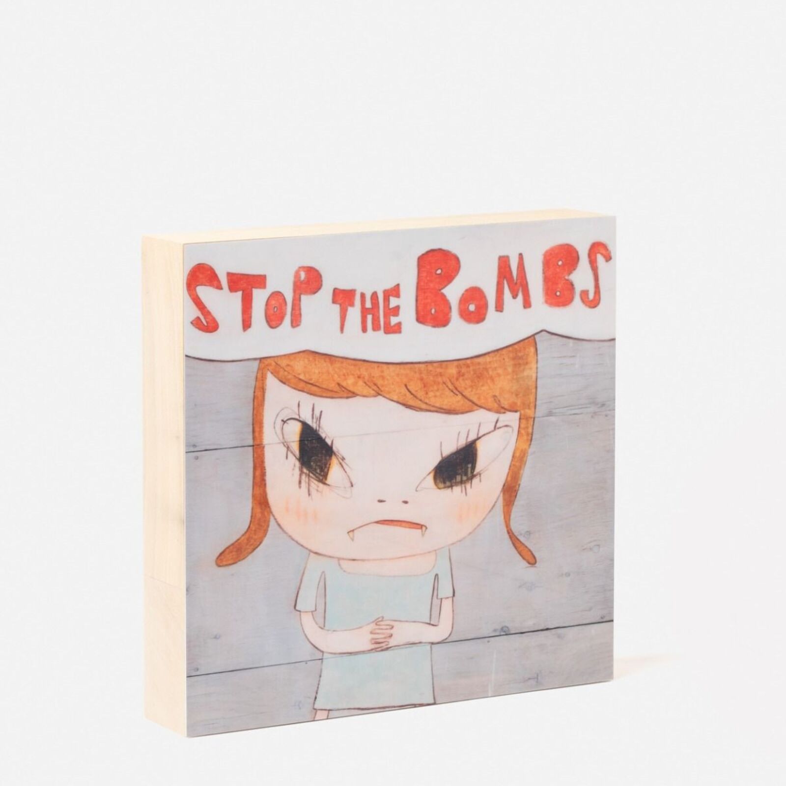 A wooden block with a drawing of a girl holding a sign that says stop the bombs.