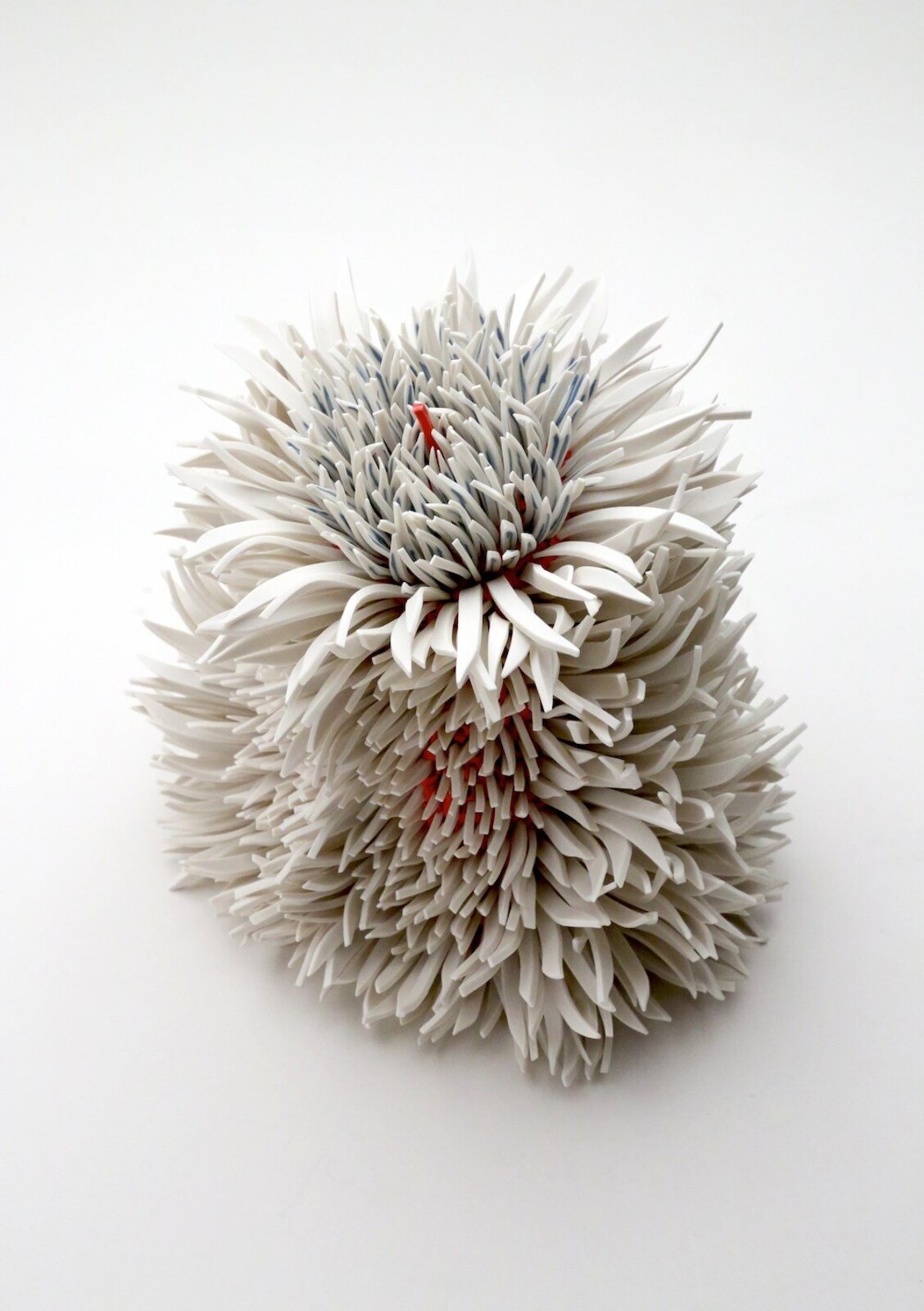 A spiky, spherical sculpture made of layered white and grey elements with hints of red.