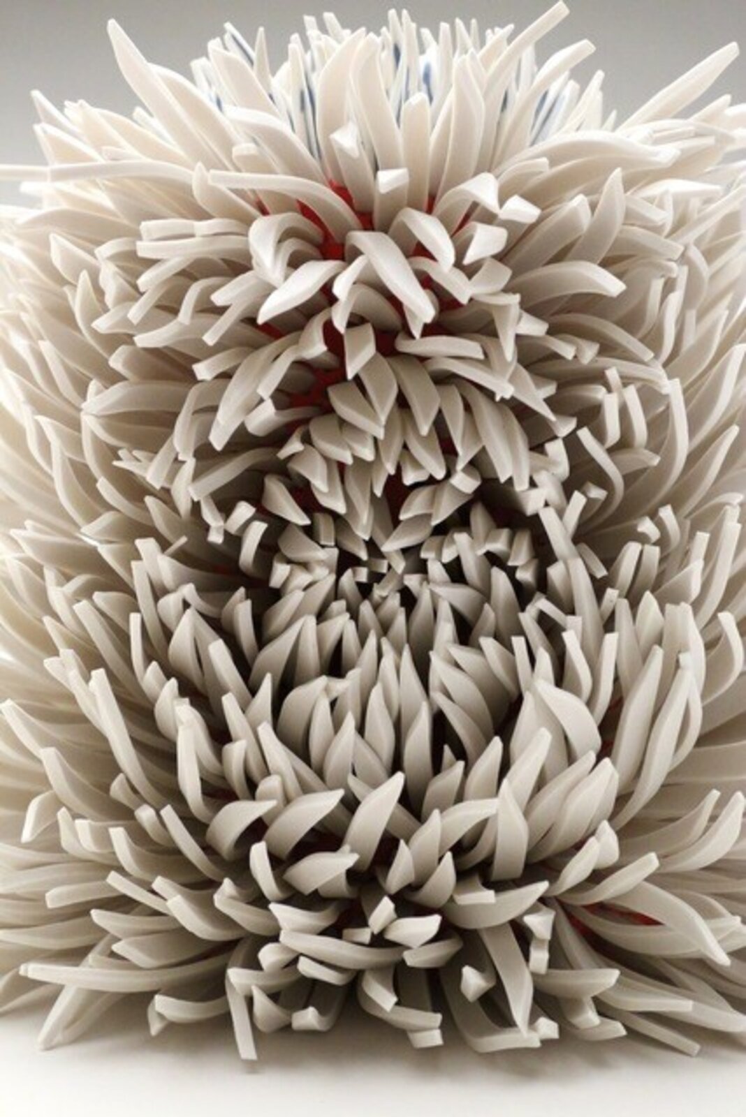 A spiky, spherical sculpture made of layered white and grey elements with hints of red.