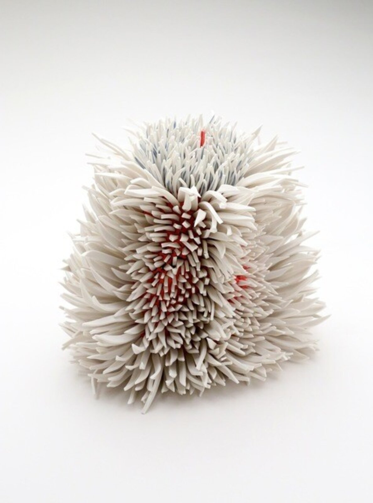A spiky, spherical sculpture made of layered white and grey elements with hints of red.