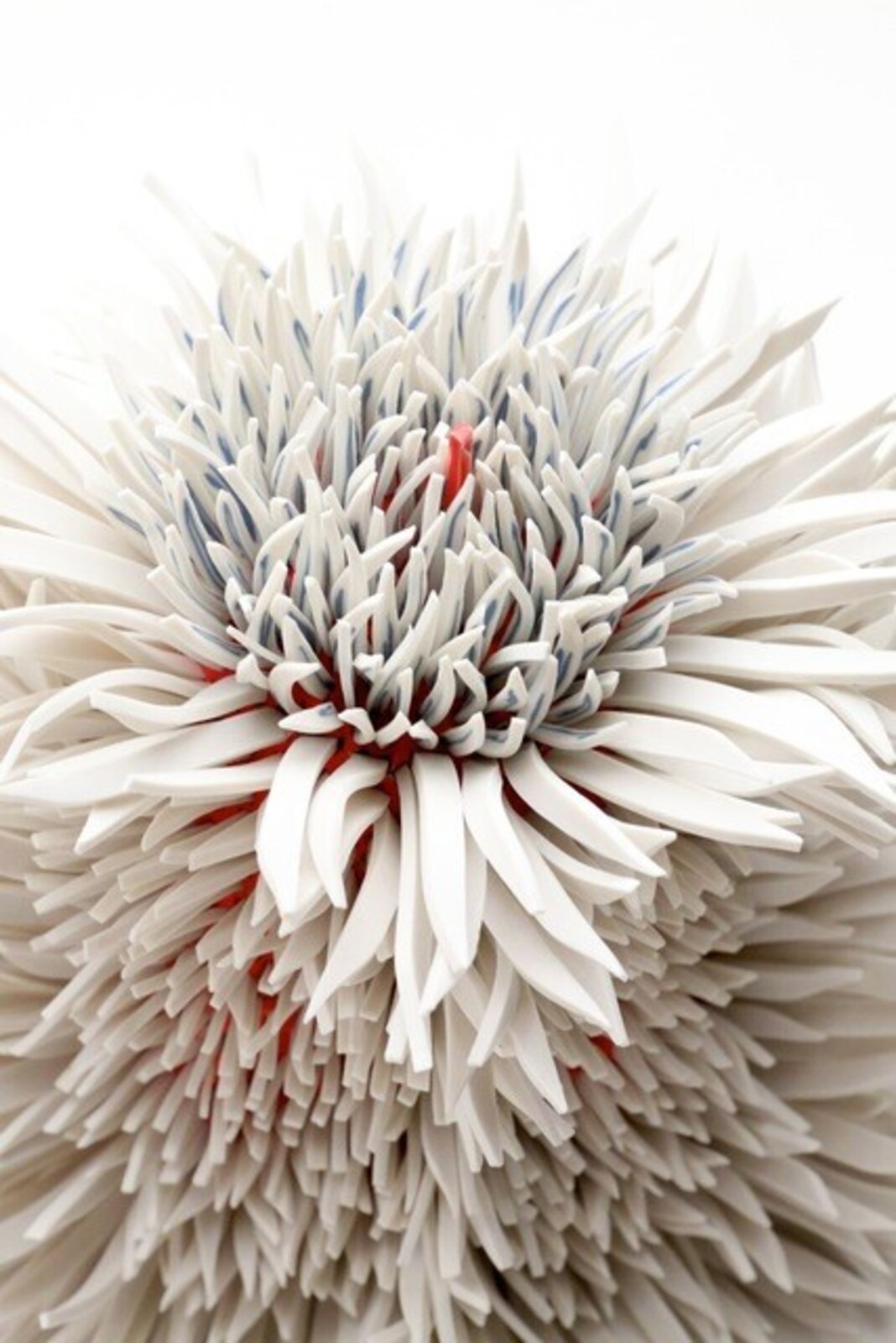 A spiky, spherical sculpture made of layered white and grey elements with hints of red.
