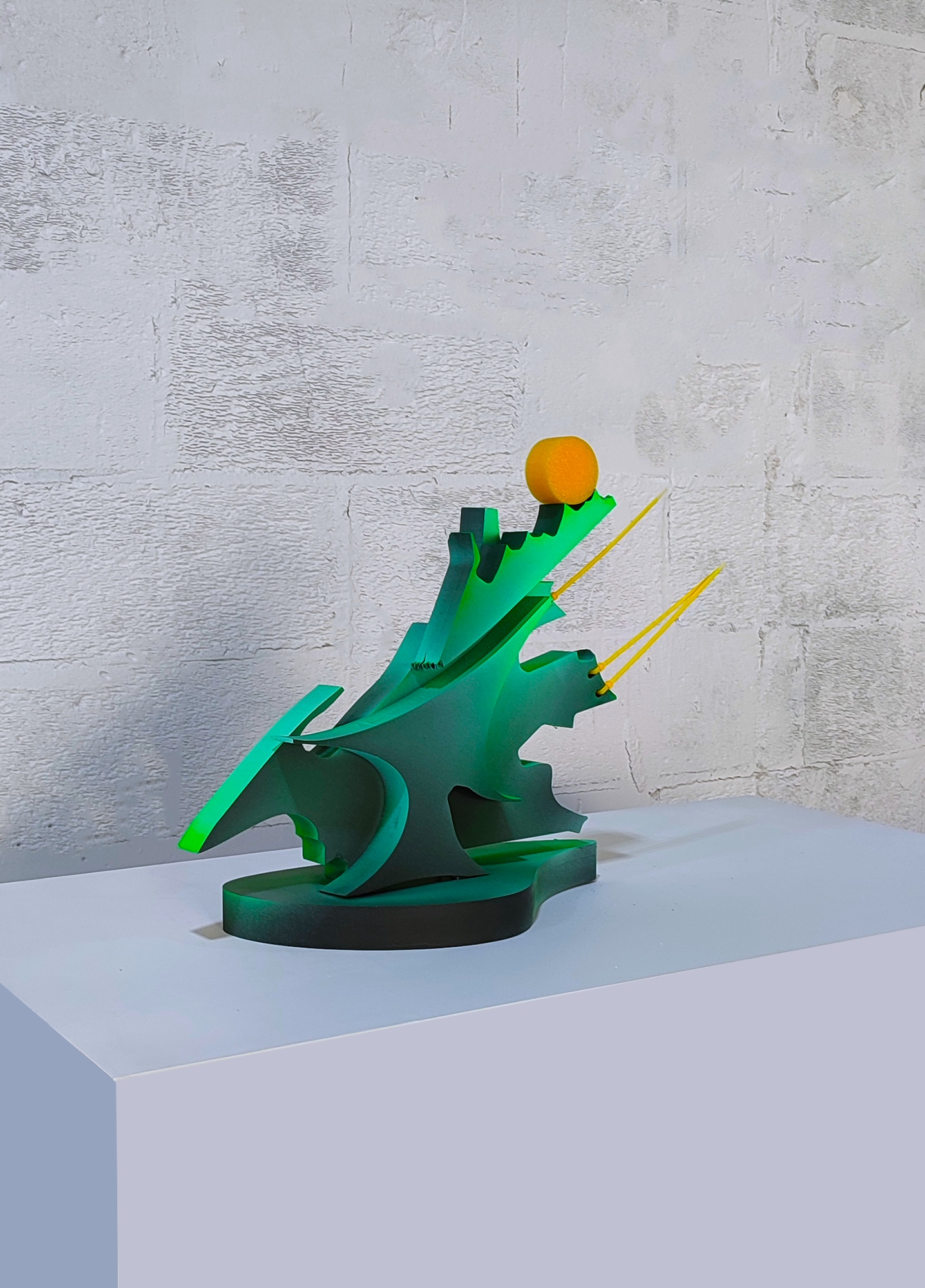 A green sculpture on a white pedestal with a yellow ball on top.