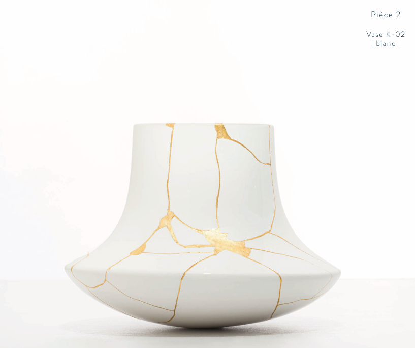 A white ceramic vase with a wide base and narrow neck, featuring a kintsugi-inspired design of gold lines tracing the cracks.